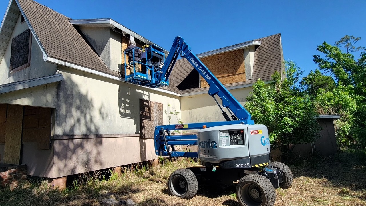 Crew using a boom lift to board up windows on a vacant Palm Coast home