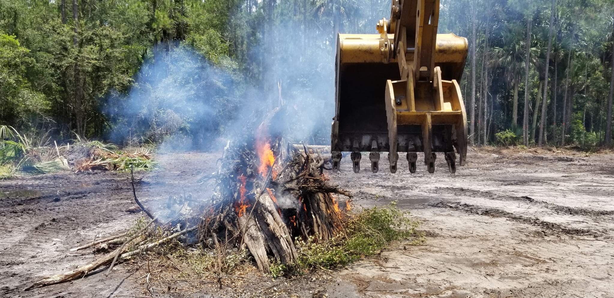 Excavator managing a controlled burn of cleared brush and stumps