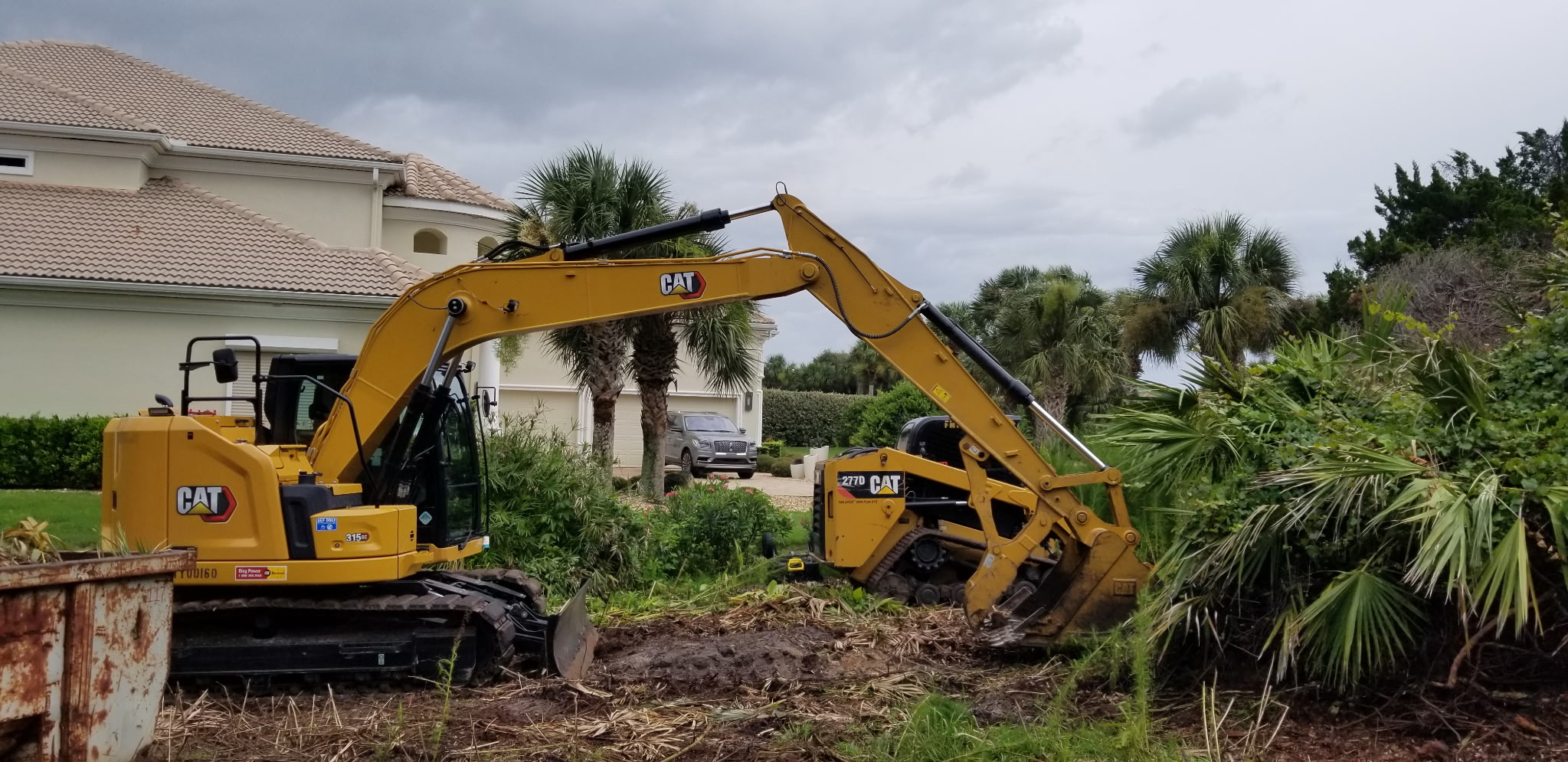 Excavator clearing dense brush and palms from a wooded Flagler County lot