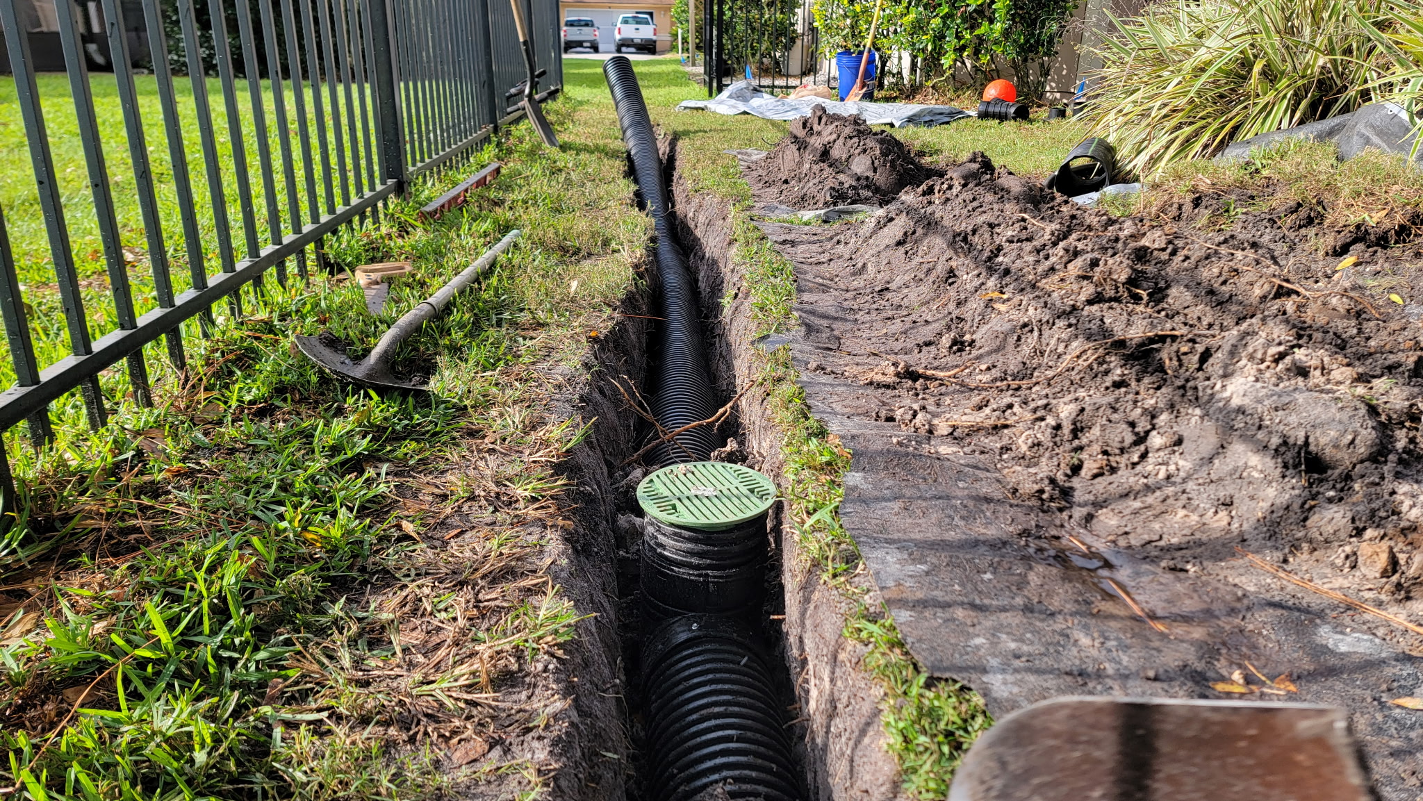 Drain trench running along a backyard iron fence with pipe and catch basin
