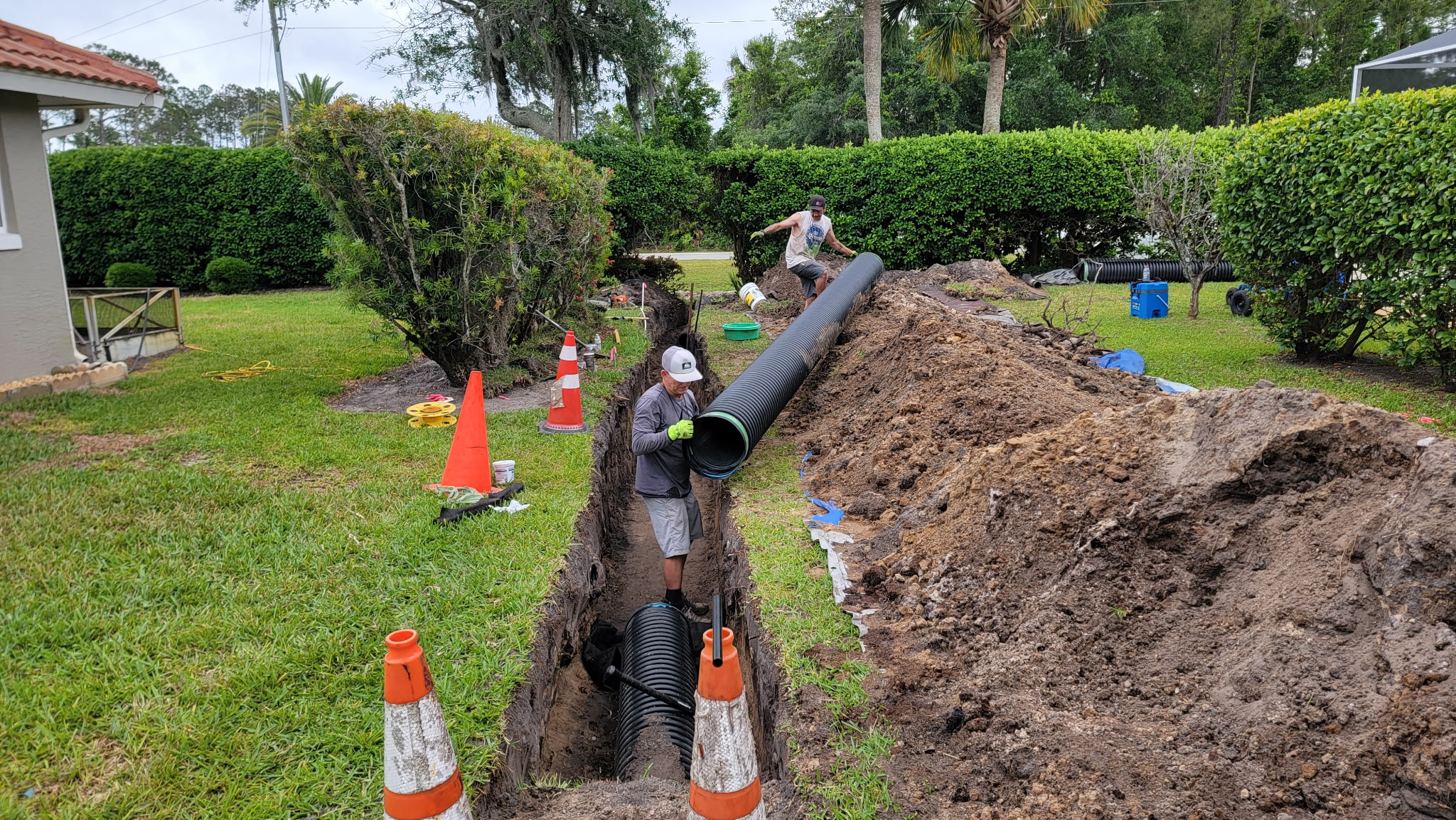 Crew lowering drain pipe into a backyard trench