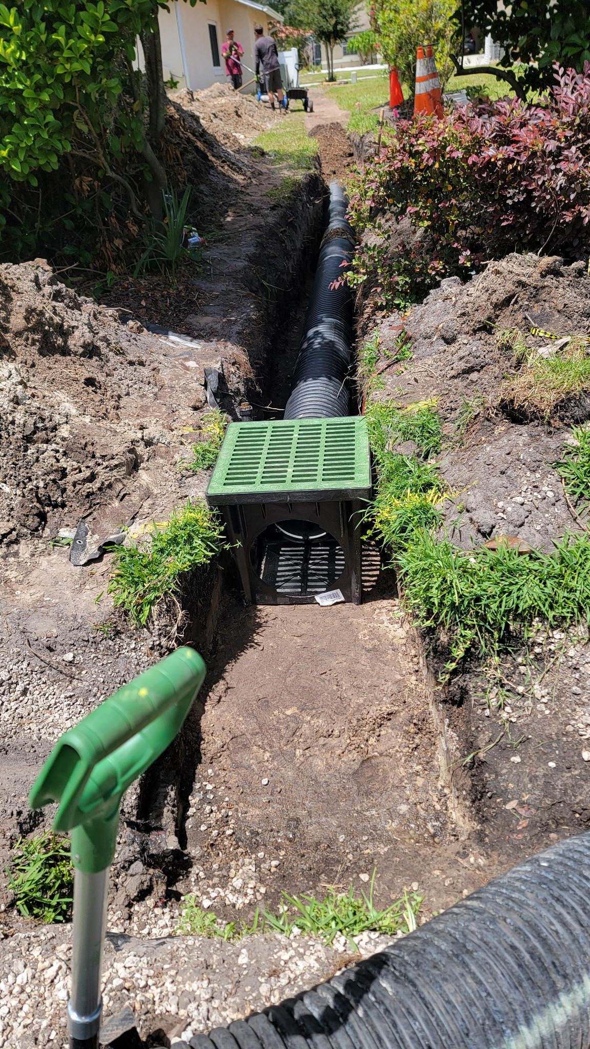 Drainage trench with corrugated pipe leading to a catch basin along a garden bed