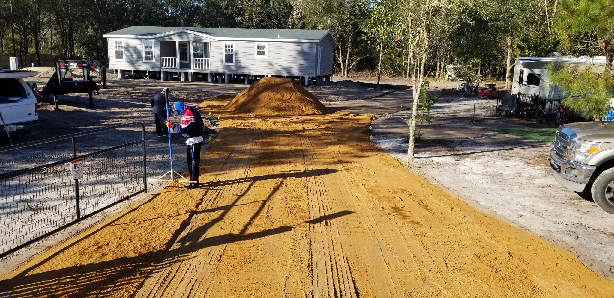 Worker hand-raking a new sand driveway smooth near a manufactured home