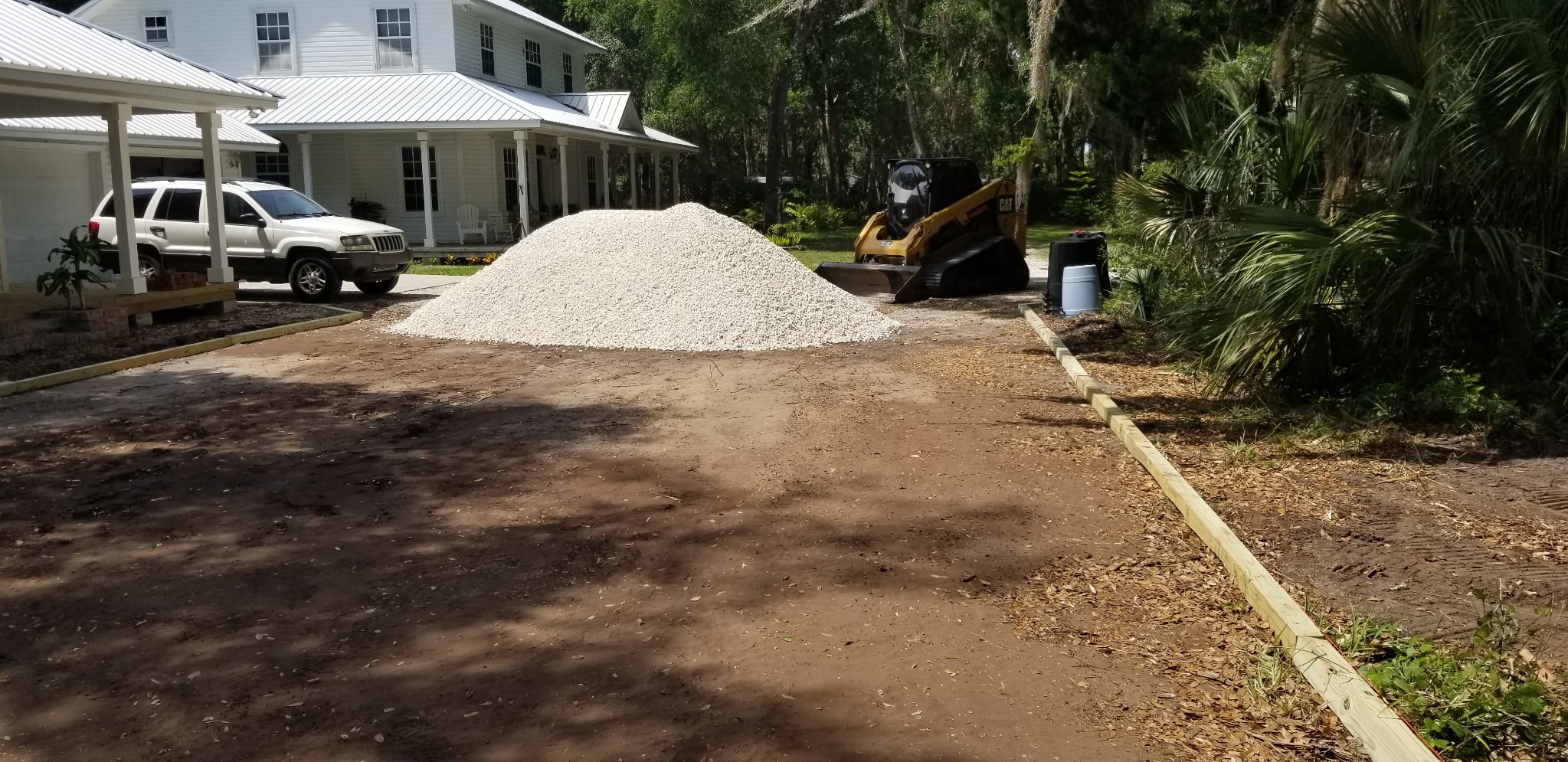 Skid steer with a pile of crushed shell at a residential driveway