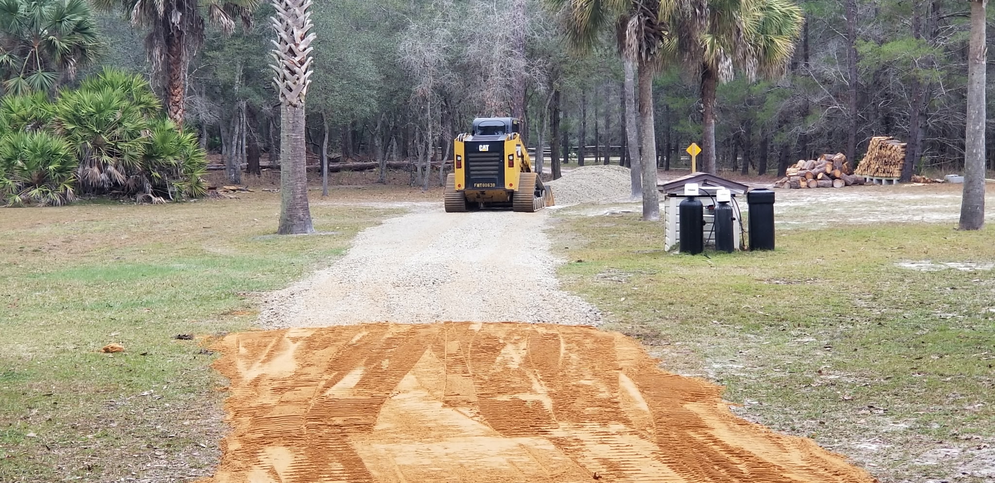 Skid steer grading a private gravel driveway through wooded property