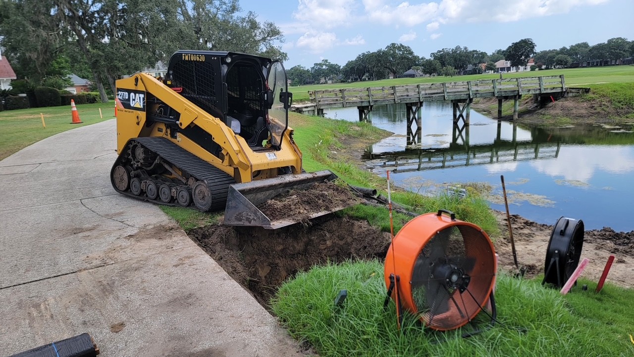 Skid steer repairing a pond bank near a golf course bridge