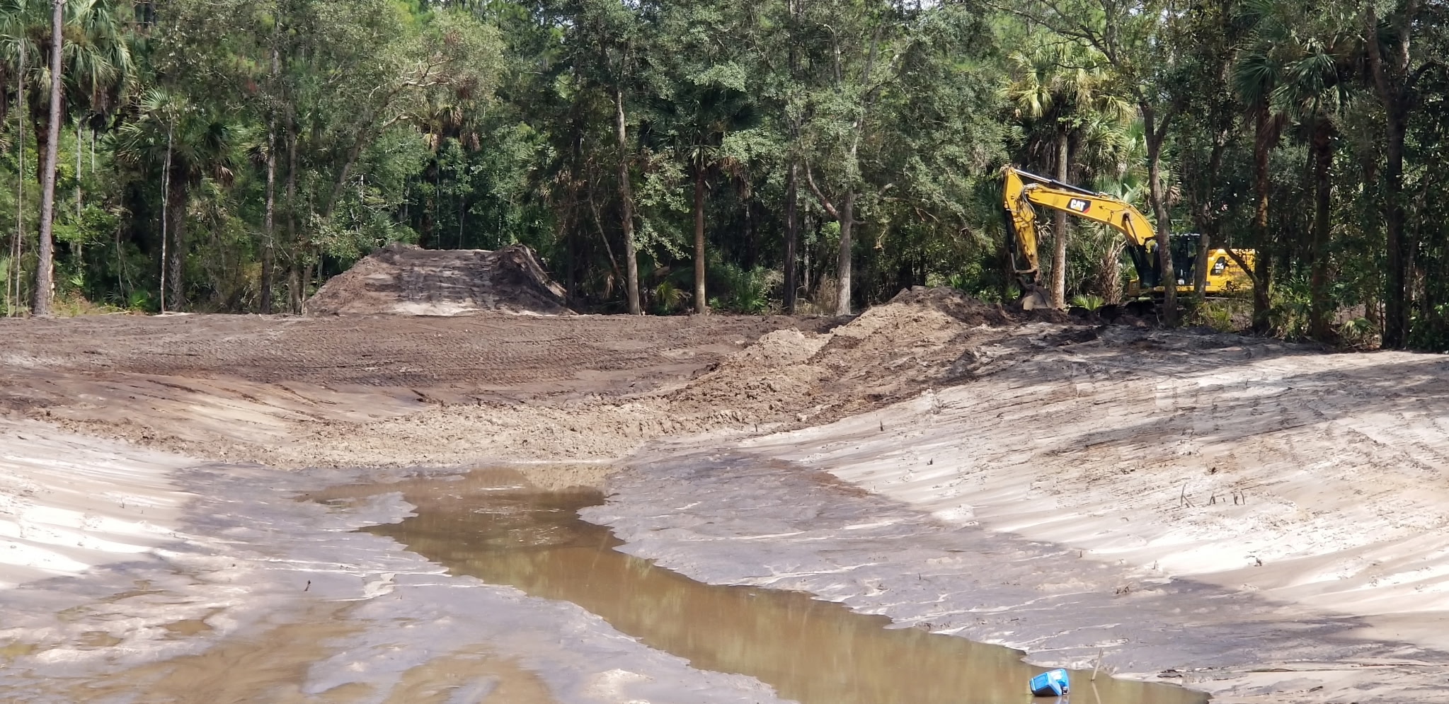 Excavator shaping a pond bank in a wooded lot