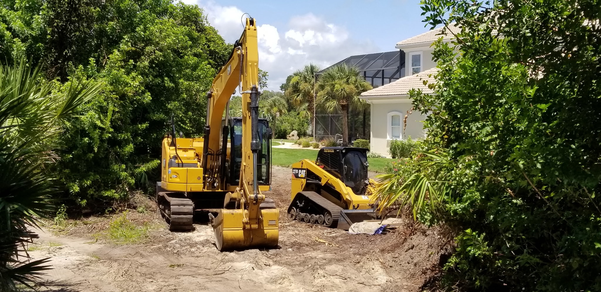 Excavator and skid steer clearing dense brush to prepare a pond site