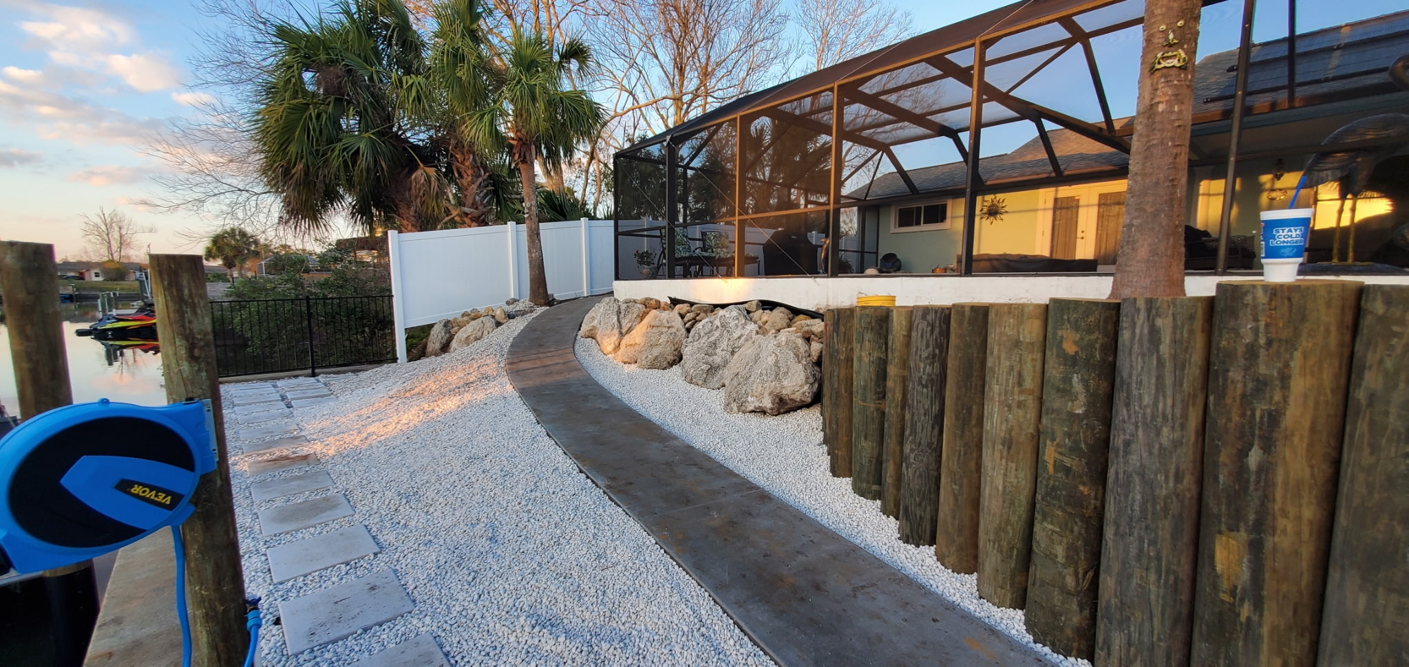 Finished paver walkway, boulders, and retaining wall on a waterfront property at dusk