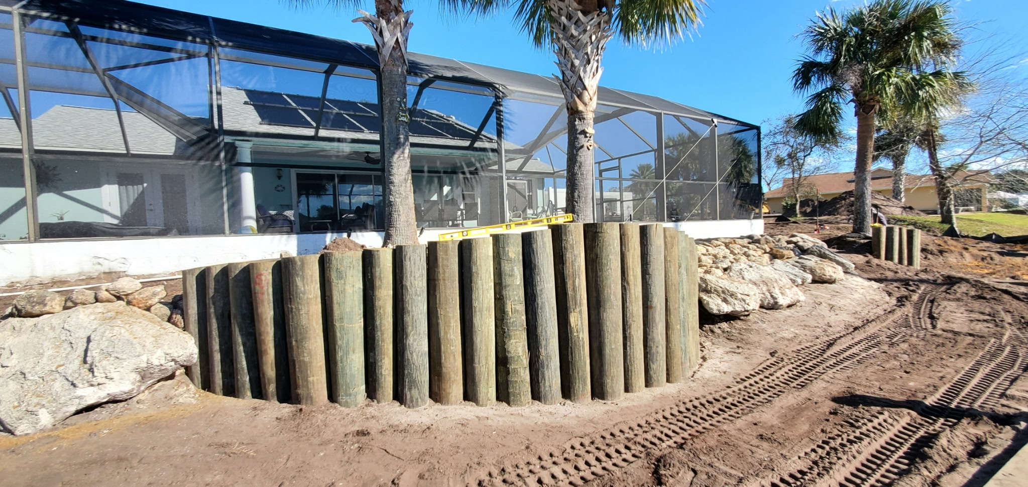 Timber pilings being leveled and set for a retaining wall behind a screened lanai